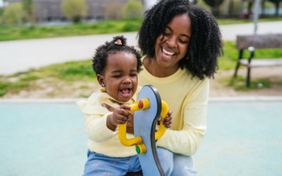 A woman and a child are sitting on a park bench. The woman is smiling and the child is holding a toy. Scene is happy and playful